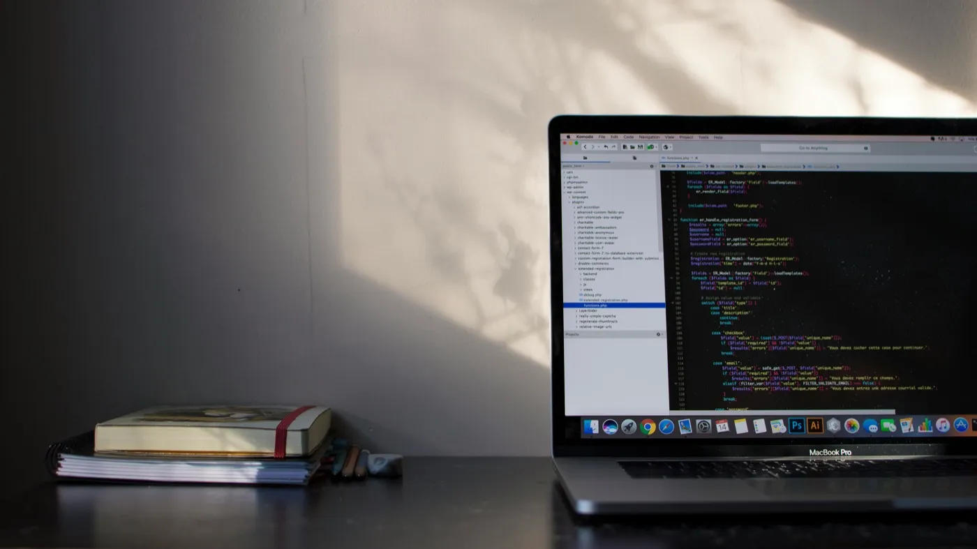 A developer's desk at night, with code visible on a laptop screen lit by a warm shaft of window light